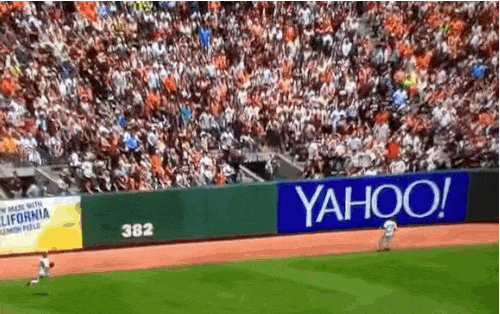 6 - Man at a baseball game behind the YaHOO sign catches a fly ball while holding a baby.