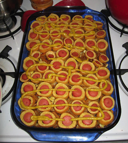 Corn Dog Casserole: Layers of hash brown patties, crumbled bacon, baked beans, corn and French fries are topped with quarter-inch slices of cooked corn dogs and drizzled with yellow mustard.