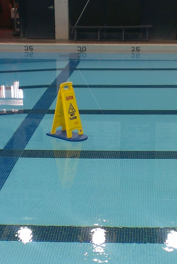 funny pictures of a floor is wet warning stand floating atop a boogie board in the pool