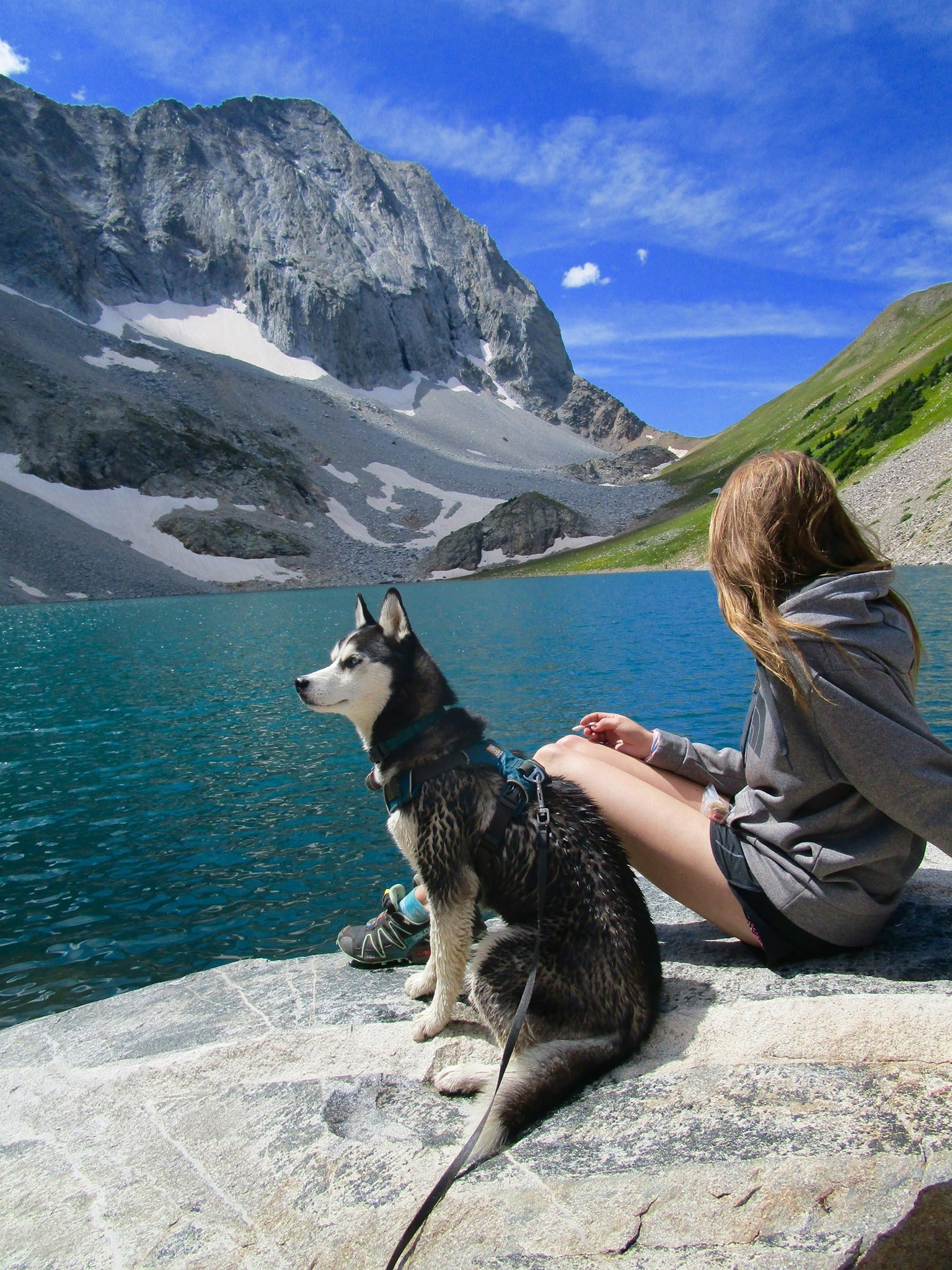 Woman and dog sitting on a rock at the edge of a glacier lake
