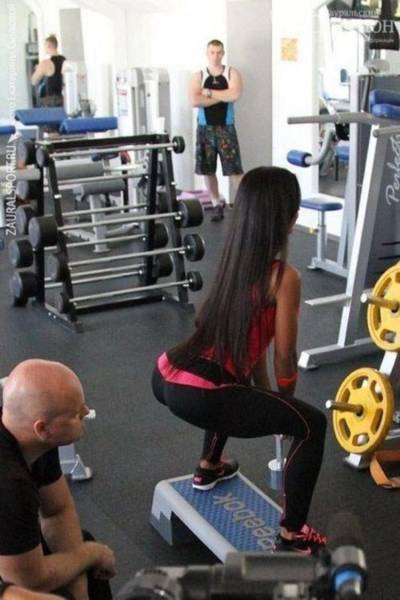 Girl doing squats in the gym with dude just checking out her butt intensely.