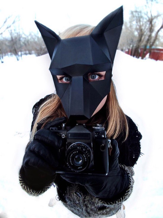 Girl with cubic shaped face mask holding a camera to take pictures in the snow.