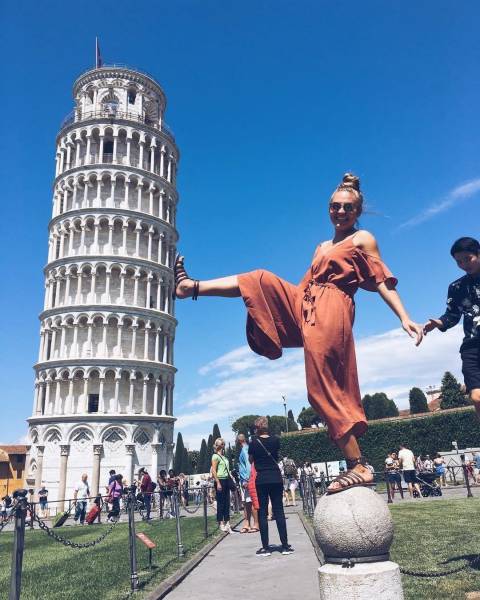 Girl posing like she is kicking over the leaning tower of Pisa.