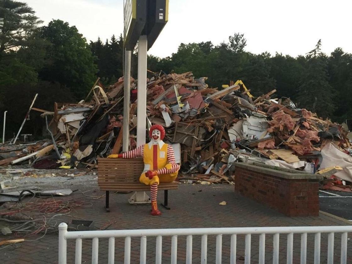 Ronald McDonald statue sitting gleefully outside an destroyed McDonalds.