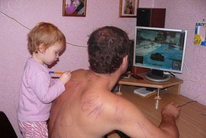 Kid is doodling on dads back as he plays on the computer