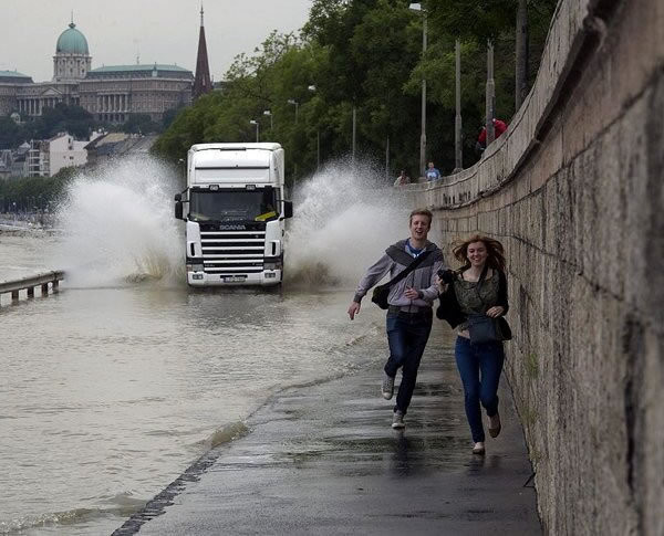 Couple running from truck that is about to splash them with puddle water.