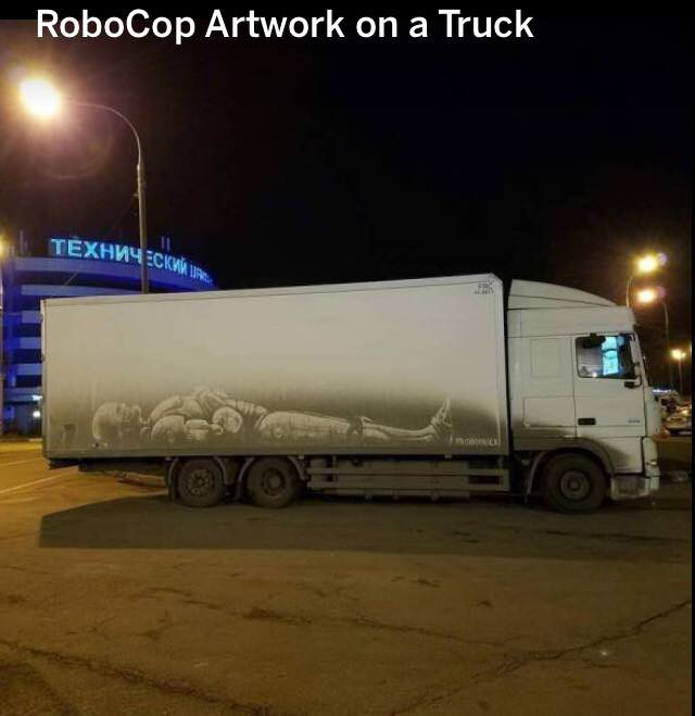 awesome artwork on the grime of a truck that looks like a sleeping robocop