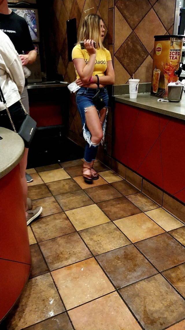 Girl waiting in line for food wearing jeans that look like they exploded at the knees