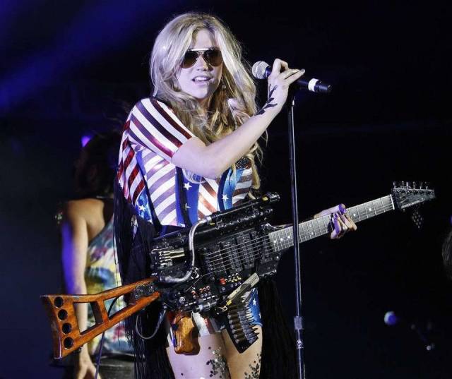 woman on stage by a mic holding a guitar that looks like an assault rifle
