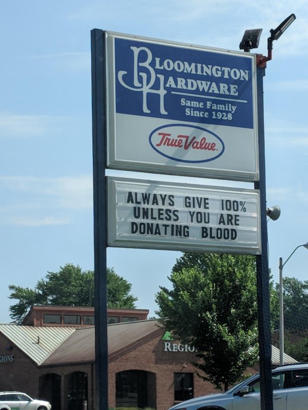 street sign - Ploomington Ardware Same Family Since 1928 TrueValue Always Give 100% Unless You Are Donating Blood Regiu. Sjons
