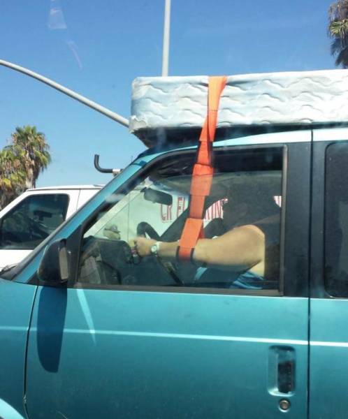 person holding down mattress with strap to his arm while driving