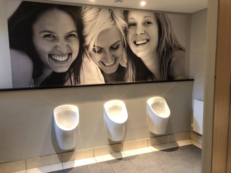 a photo of 3 women looking down laughing in a mens bathroom over the urinials