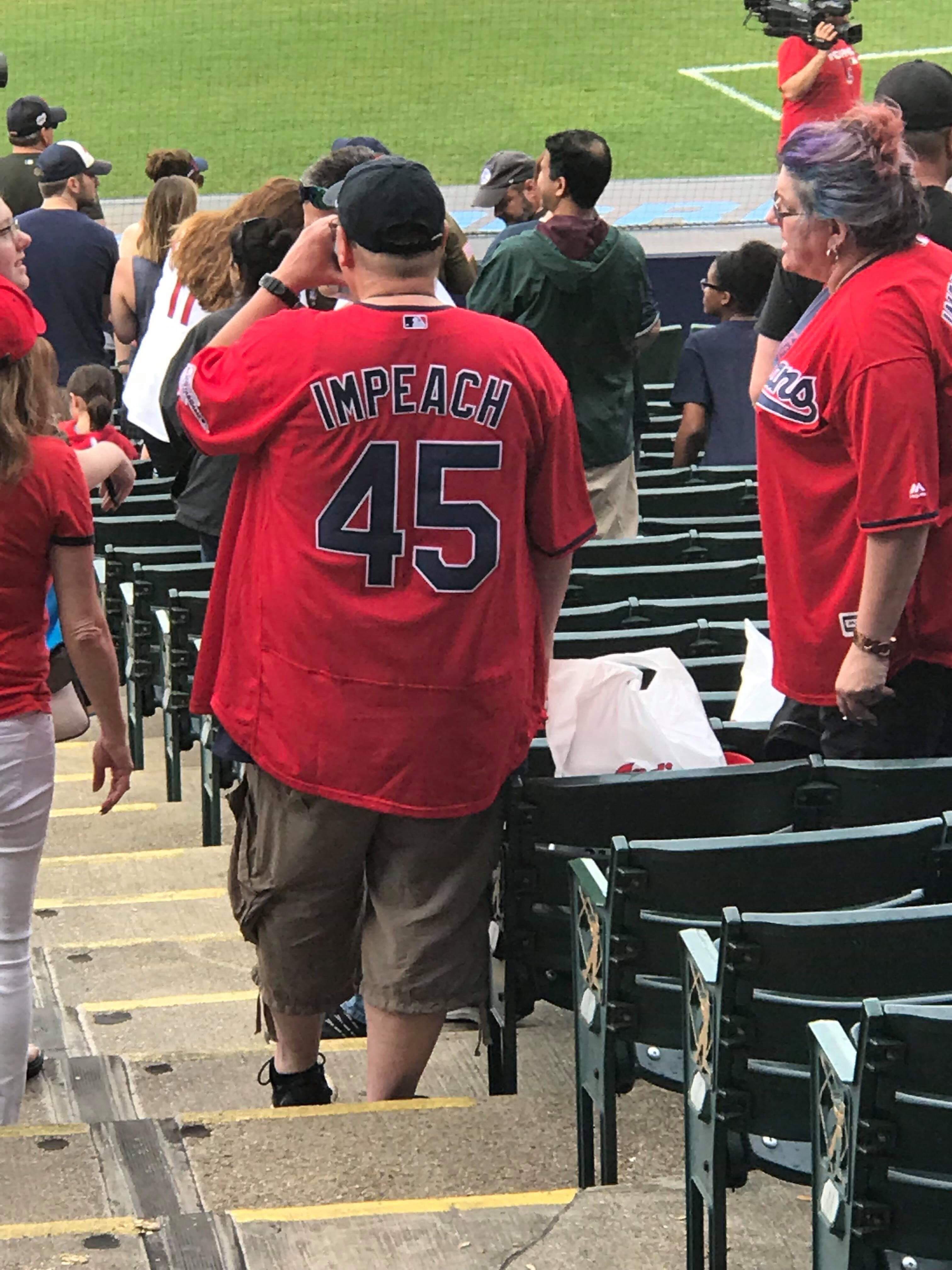 Baseball fan wearng a shirt that says Impeach 45