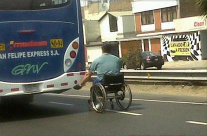 guy in wheelchair holding onto a bus rolling down the street getting towed