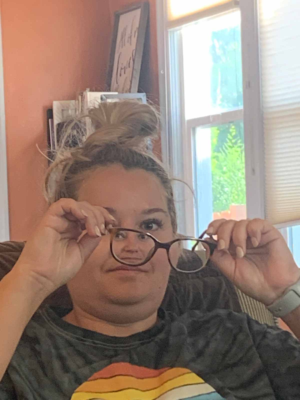 Funny photo of a woman with her glasses in front of her face so her head looks tiny in one of the lenses