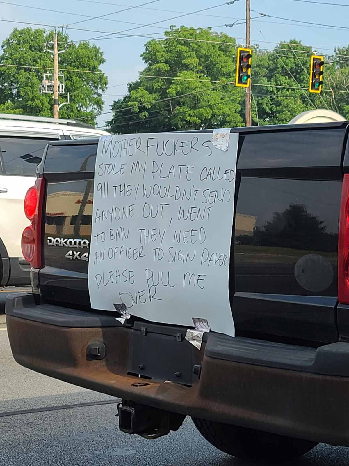 Funny handwritten sign on the back of a Dakota 4x4 that says 'motherfuckers stole my plate called 911 they wouldn't send anyone out, went to BMV they need an officer to sign paper please pull me over'