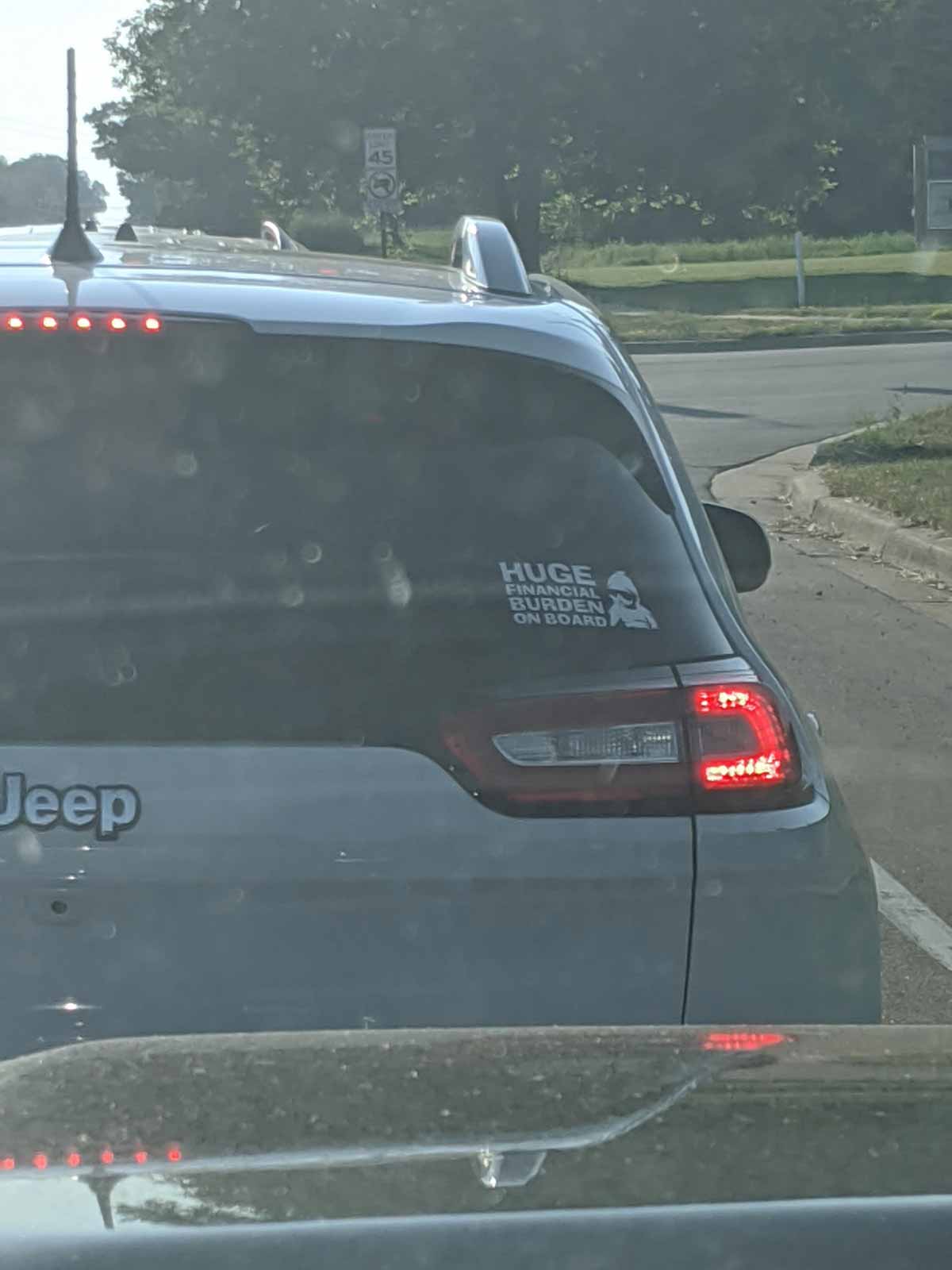 Funny sticker on the back of a jeep that says 'huge financial burden on board' and a picture of a baby