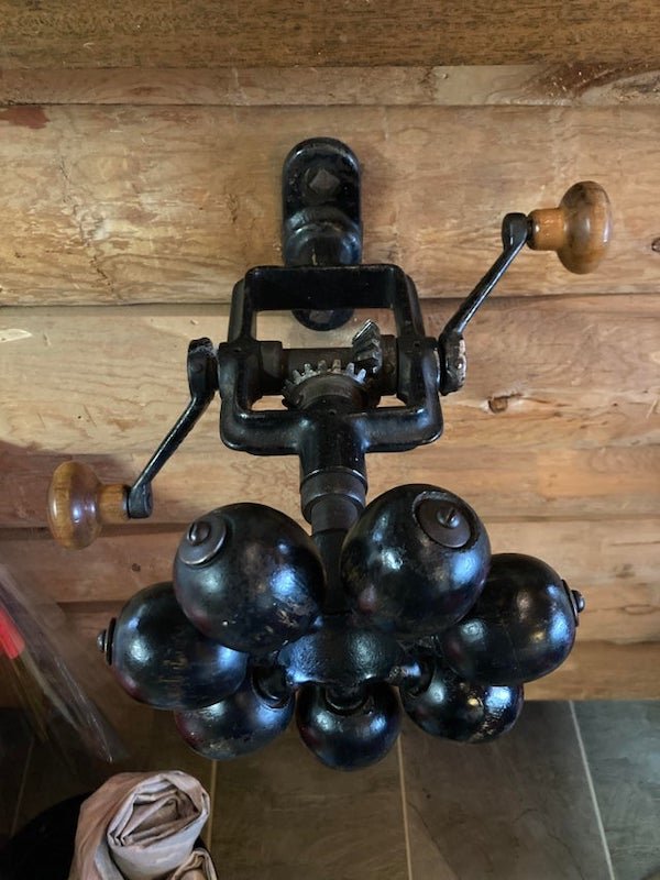 Mixer, back massager??? Mounted on wall at cabin on Hood River OR. Two handles spin the seven arms with wooden balls. Wooden balls spin freely. A: Rope winder. Each head would hold a twine string, the spin would then wind them together.