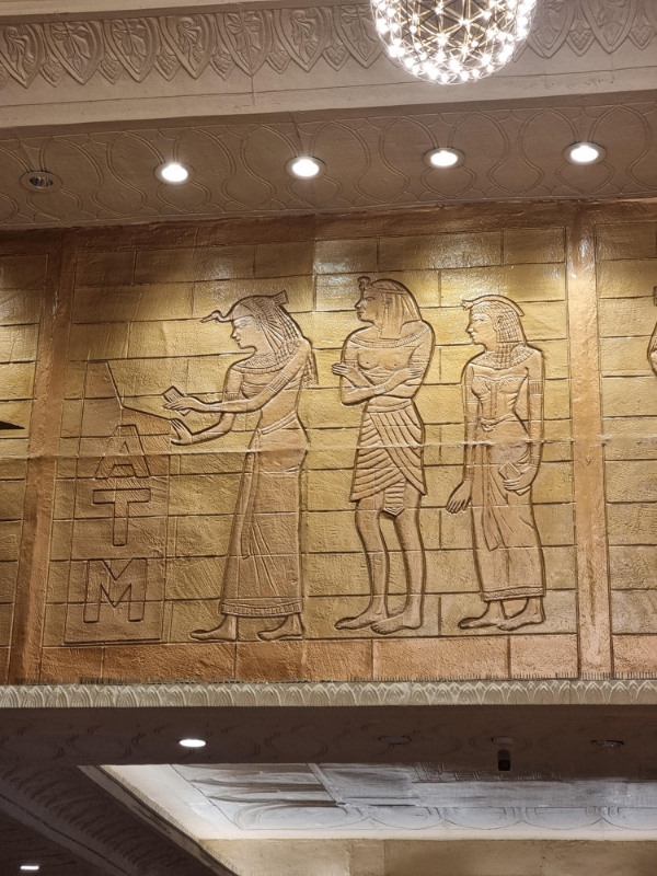 “This pyramid themed shopping mall has a wall of pharaohs waiting in line to access an ATM.”