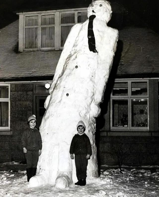 Scotland, 1963. Two kids stand in front of their 17-foot snowman.