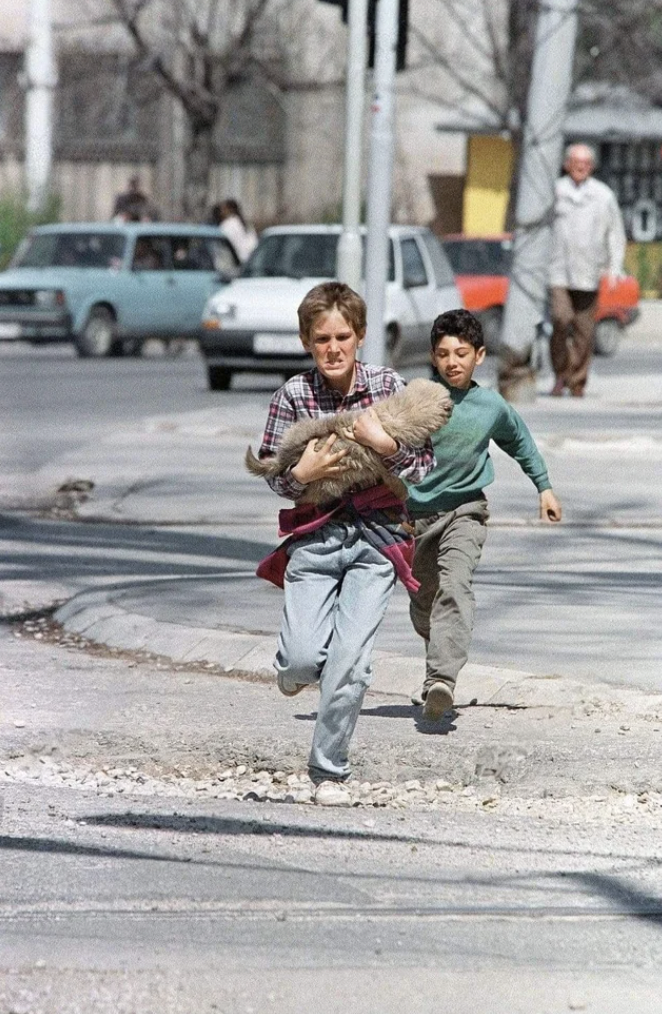 A boy carrying his dog while crossing the infamous “Sniper Alley.” April, 1995.