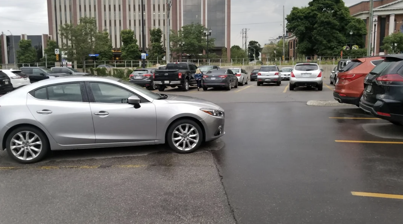 “This car parked in the middle of the parking lot between faded parking lines.”