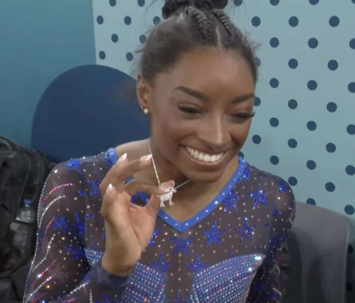 Simone Biles showing off a diamond-encrusted goat necklace after winning her 6th Olympic gold.