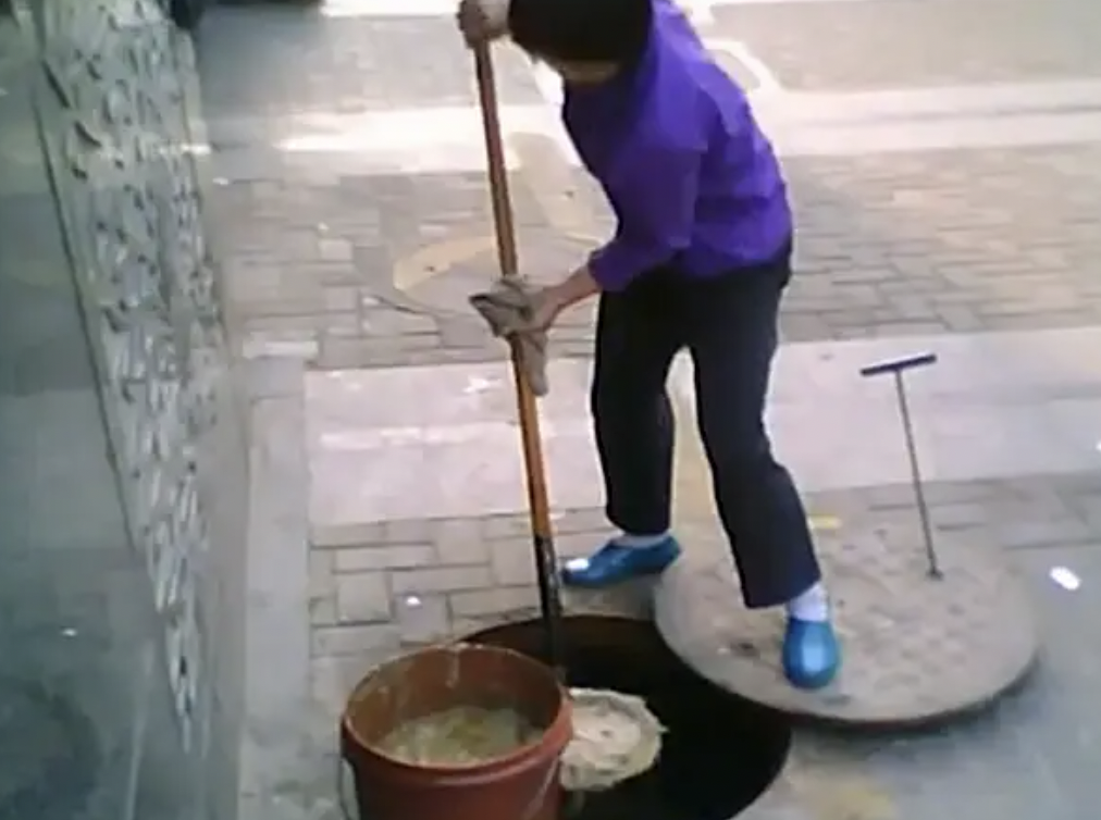 Street vendor in China opening a manhole cover to make her “gutter oil.”