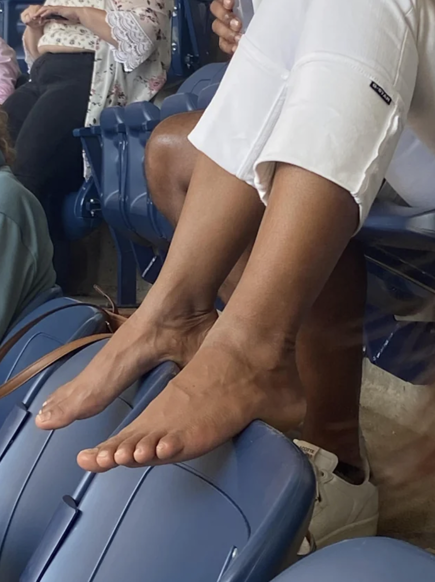 “Woman putting her bare feet on the seats at the US Open.”