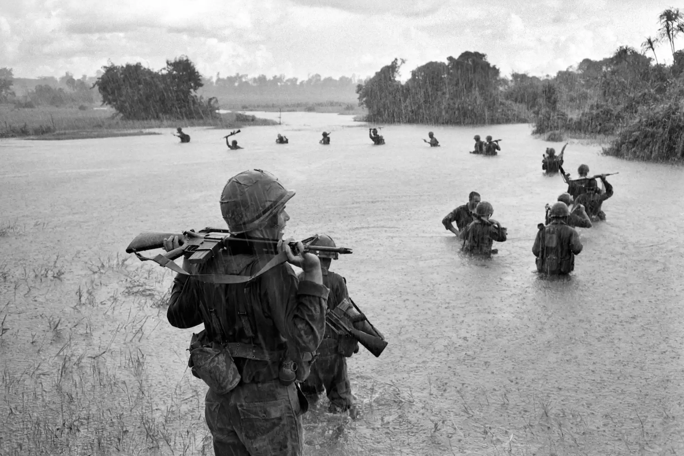 US paratroopers of the 2nd Battalion, 173rd Airborne Brigade, hold their automatic weapons above water as they cross a river in the rain.