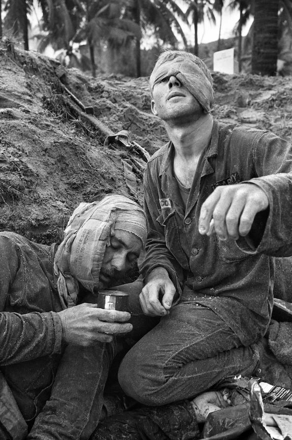 Medic Thomas Cole looks up with his one unbandaged eye as he treats wounded Staff Sergeant Harrison Pell during a firefight on 30 January 1966.