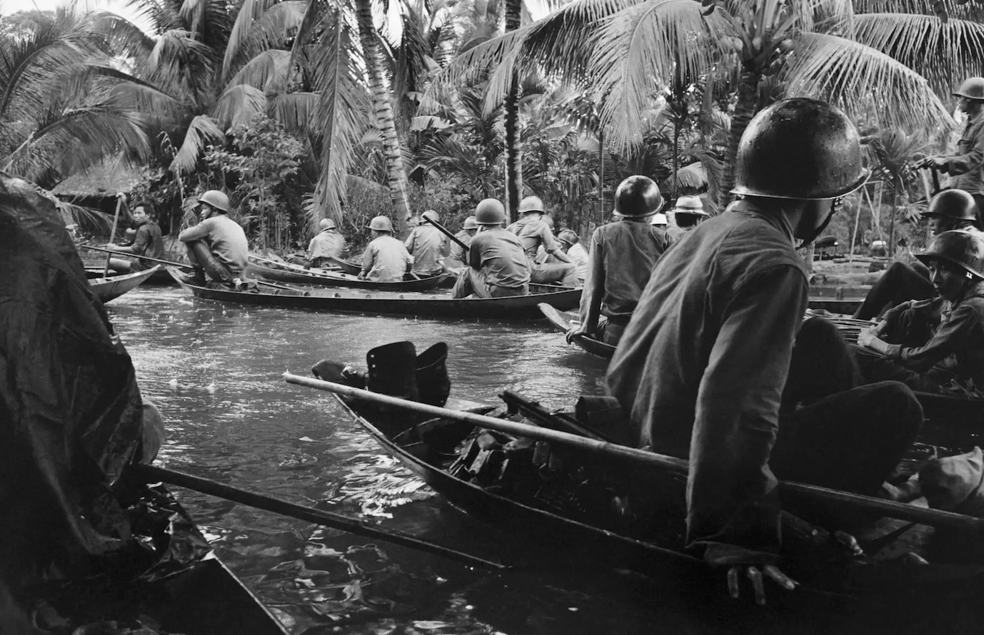 Caught in a sudden monsoon rain, part of a company of about 130 South Vietnamese soldiers moves downriver in sampans during a dawn attack on a Vietcong camp on 10 January 1966.