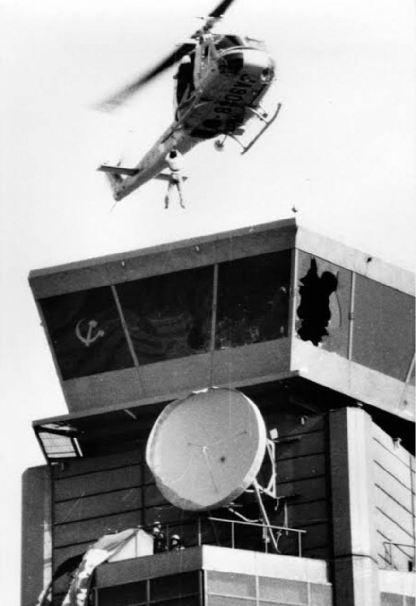 A police helicopter evacuates staff members who escaped from the roof of an airport control tower in 1978, as airport construction opponents who occupied the tower raise a hammer and sickle flag. Chiba Prefecture, Japan.