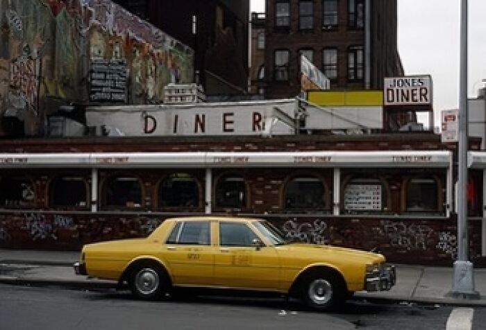 An iconic yellow taxi cab parked out front of a Diner in 1990.