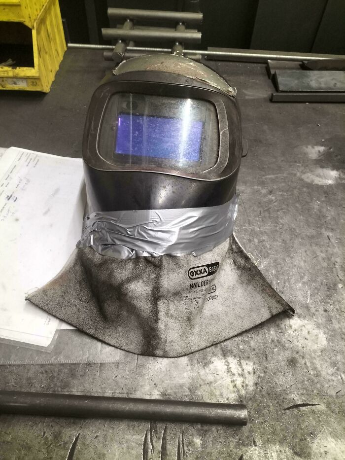 This welder was tired of catching sparks to the neck so they taped an old glove to the mask.