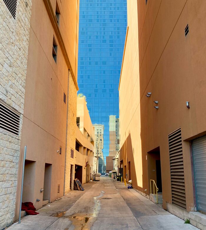 This alleyway next to a glass skyscrape gives the appearance of a very long alleyway with the sky behind it.