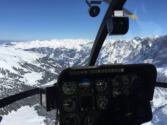 The cockpit of a MD520 helicopter flying over the mountains.