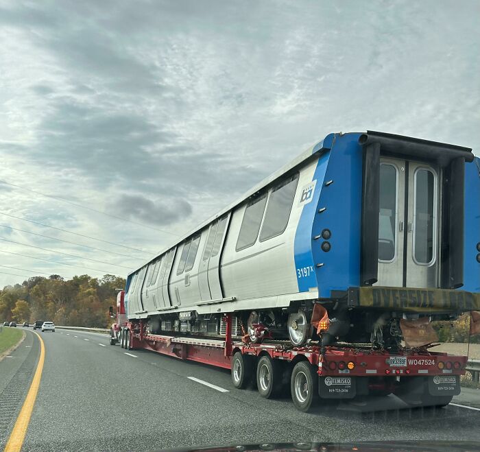 A passenger metro train hitching a ride on the back of a truck.