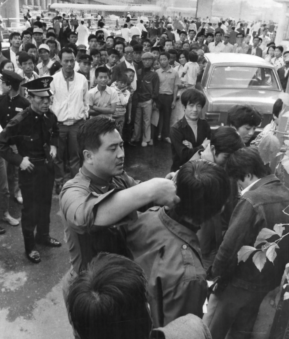 People watching policemen inspect long hair. Those caught had their hair cut on spot.