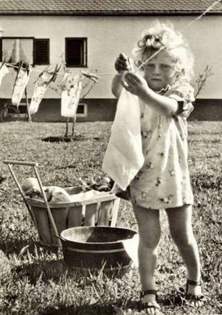 A young girl hangs clothes on a clothesline in the 1950s.