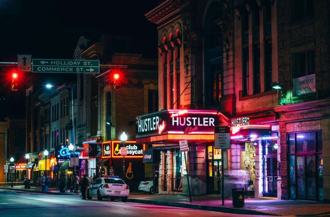 The neon streetlights are buzzing like a heartbeat that no one hears.