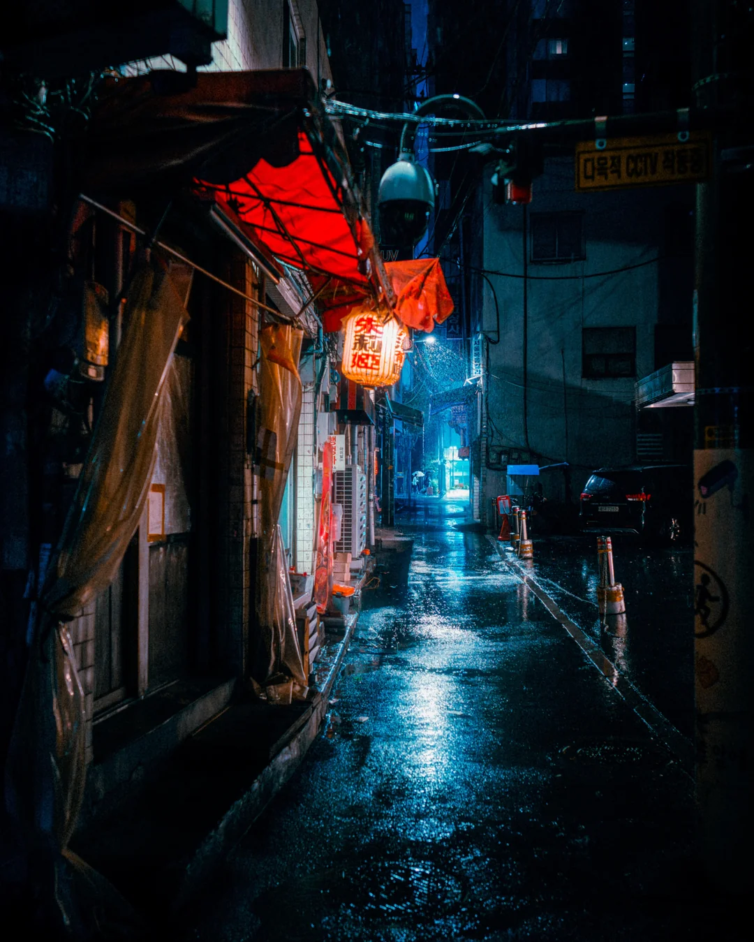 Red lanterns whisper to the wet pavement with the lingering rain.