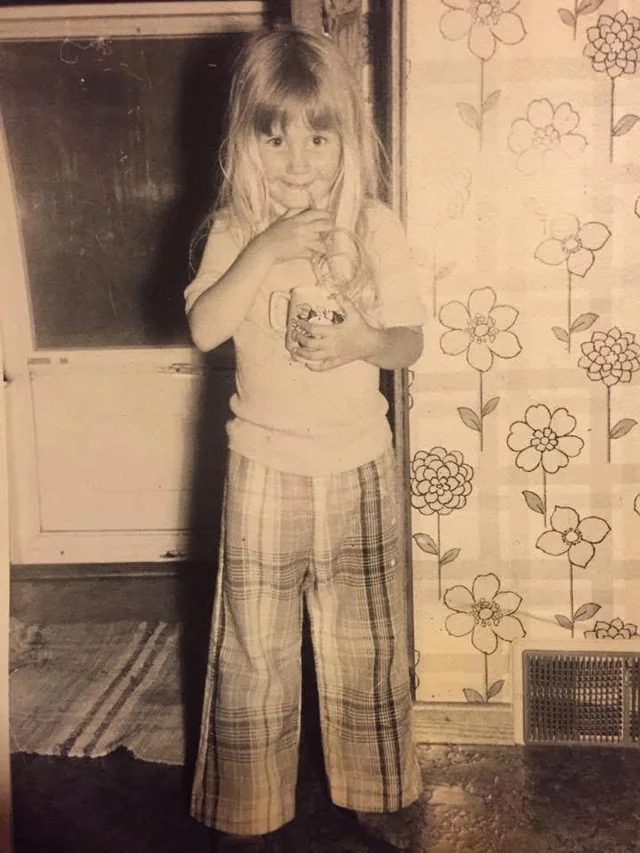 Plaid pants, patterned wallpaper, and a shy smile.