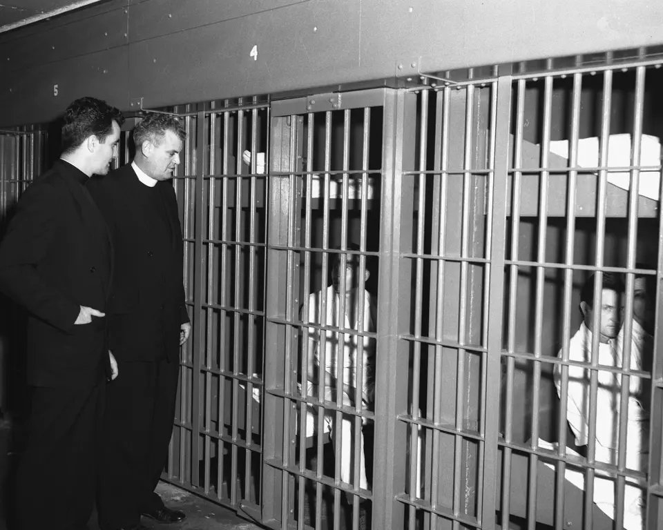 Two priests peer into barred cells, moral guidance was once central to prison life.