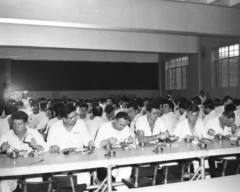 Dozens of inmates eat next to each other, showing the regimented order of daily life.