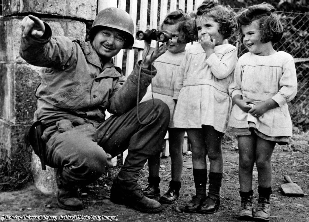 A soldier shows the planes overhead to the young kids.