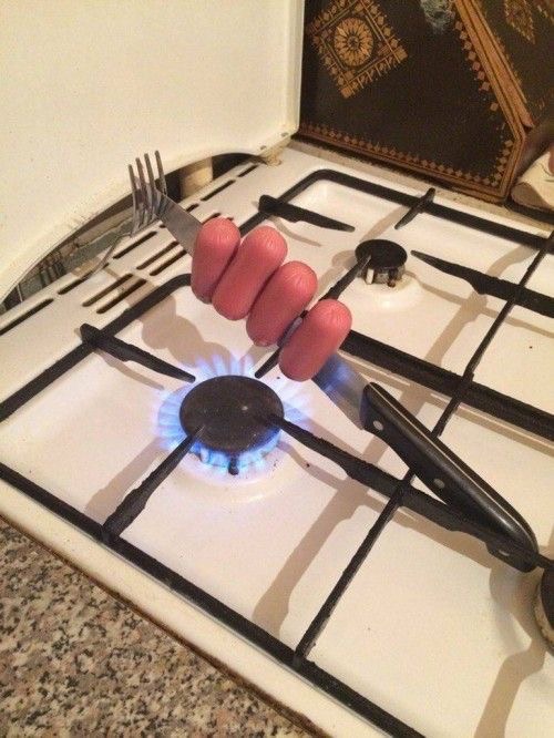 Sausages Roasting on a Knife Over a Stove 