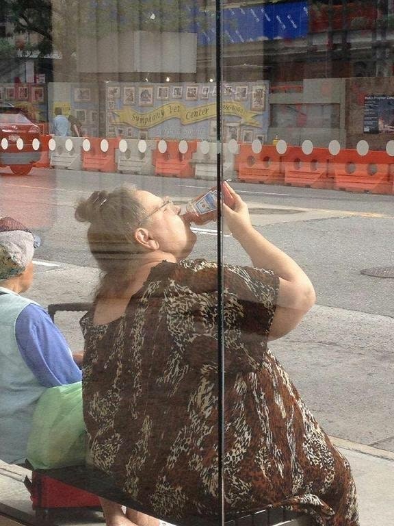 Large woman at a bus stop wearing a moo moo and drinking ketchup