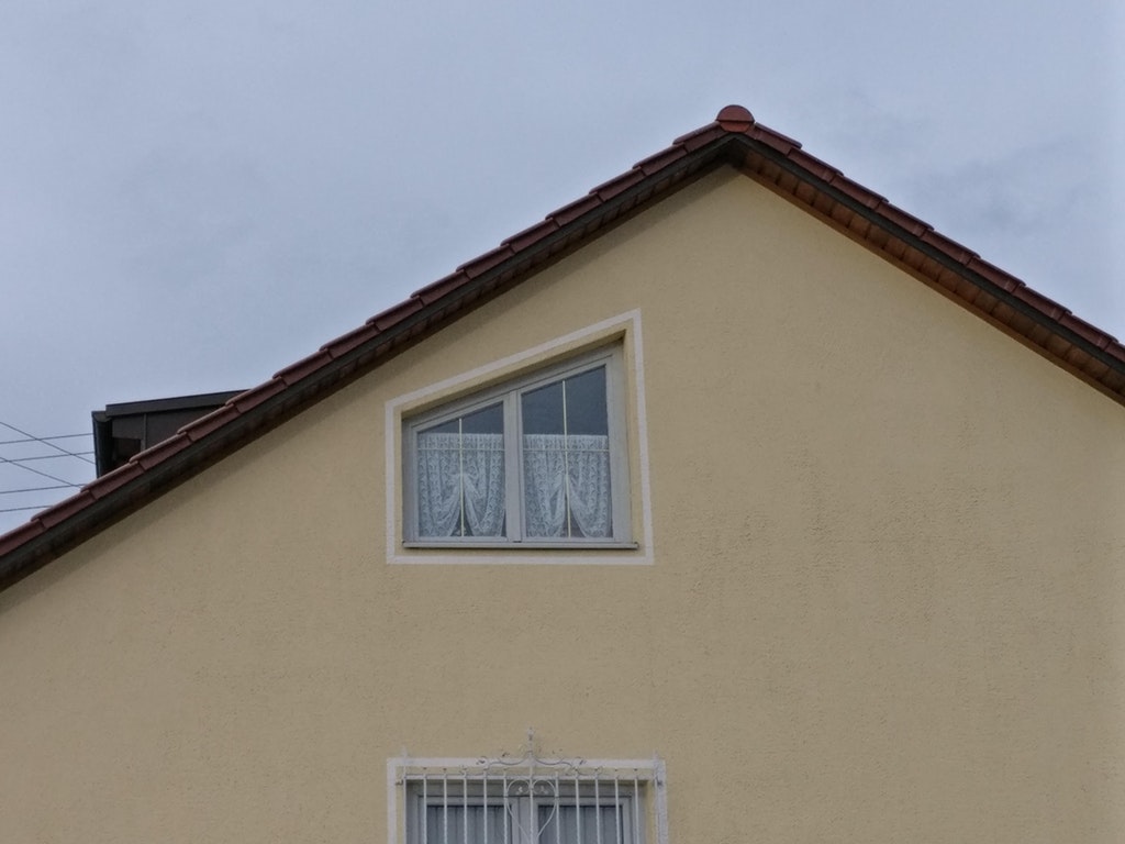 Diagonal window that is at a different angle than the roof and has horizontally mounted curtains.