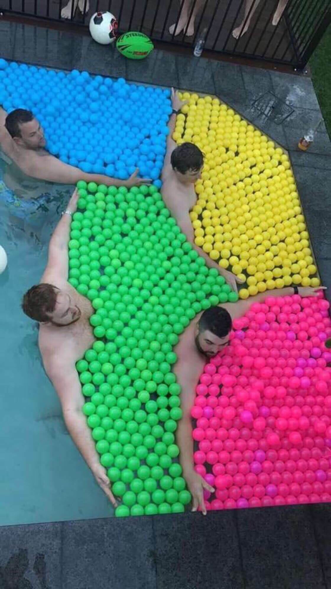 strange image of men holding balls of various colors together in swimming pool